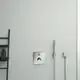 Chromfarbener Thermostat von Ideal Standard an einer hellen Wand, neben einer Handbrause und einem Wandregal mit Badezimmerprodukten.